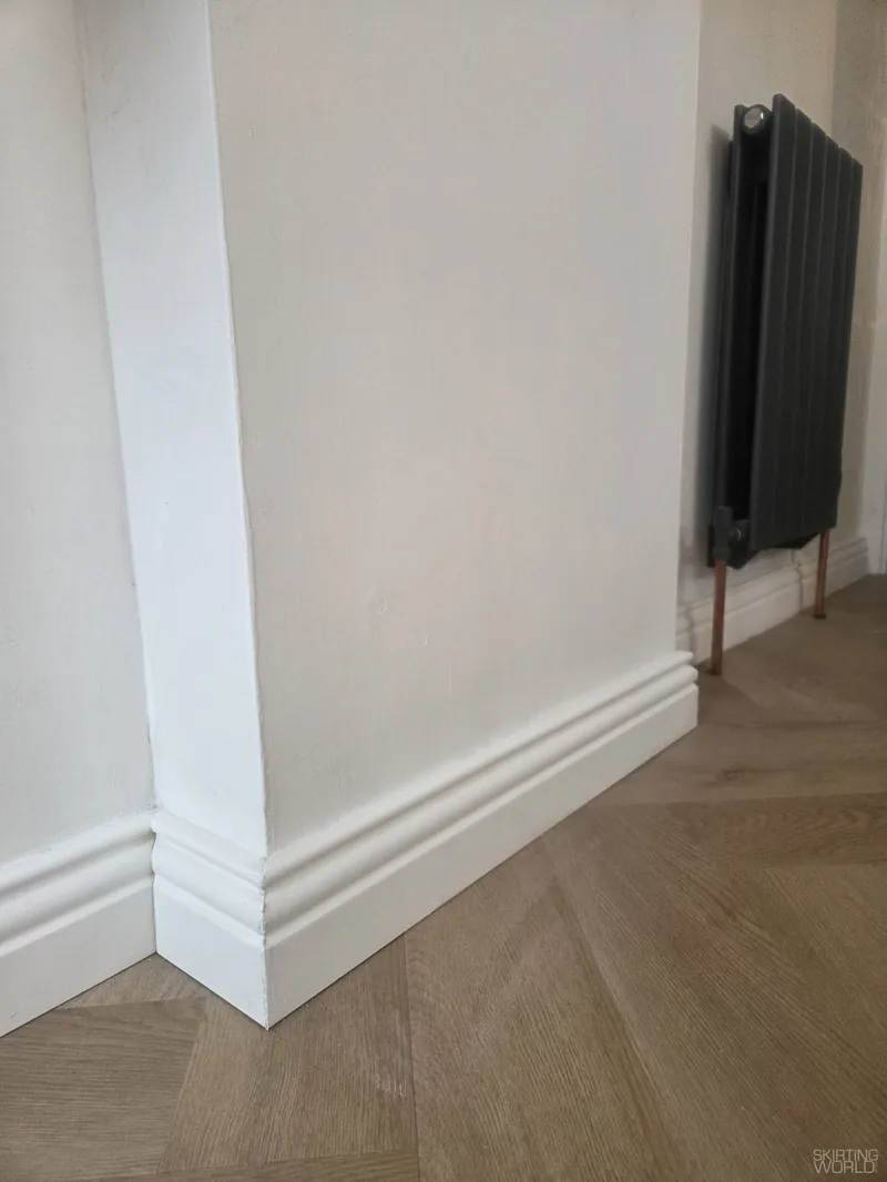 Tall Regency pine skirting board painted white above a herringbone floor.